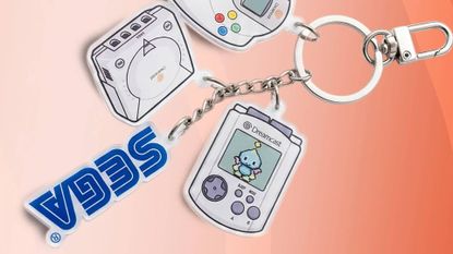 Sega Dreamcvast keychain set with VMU, Sega logo, Dreamcast console, and controller on orange backdrop.