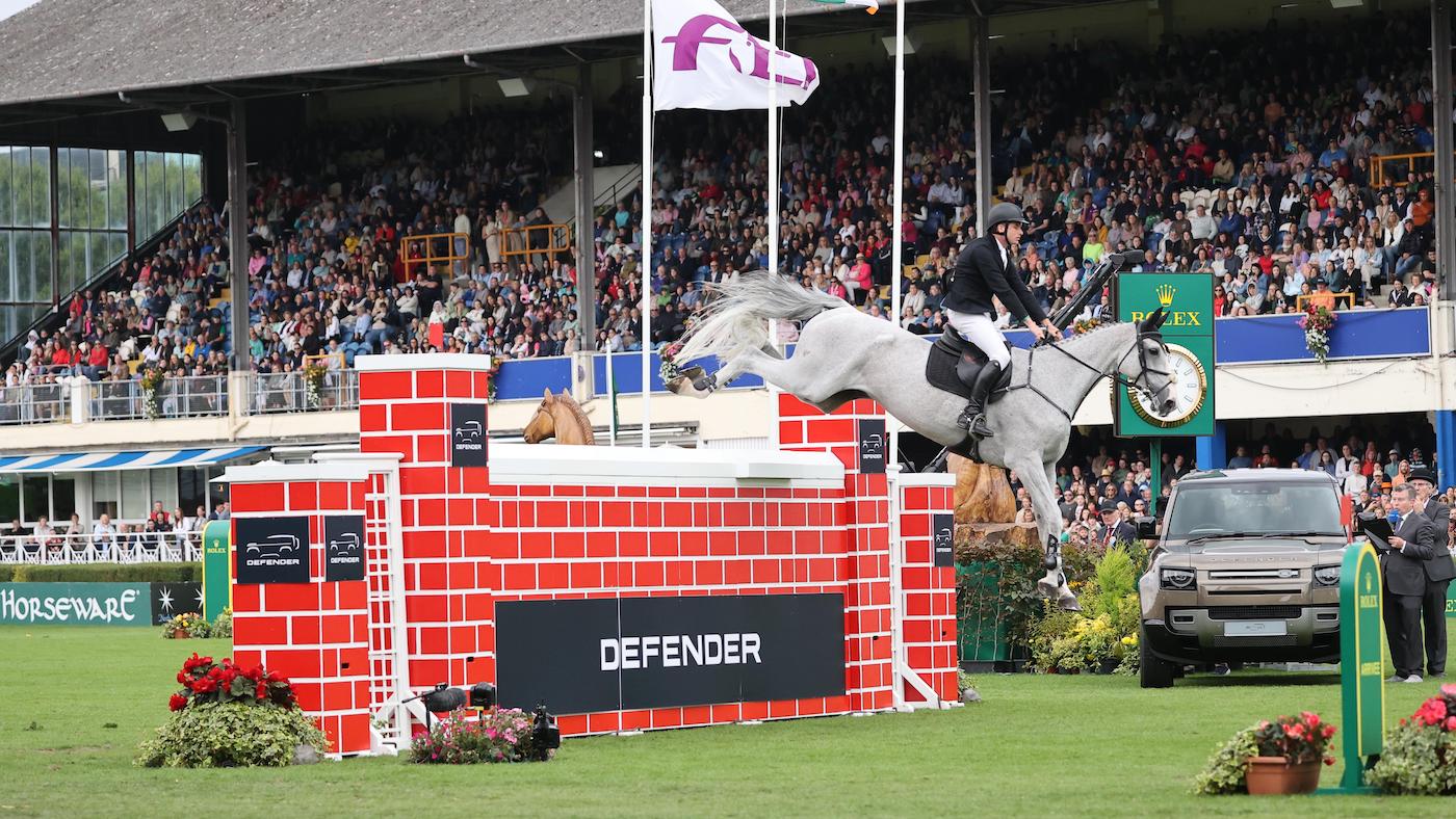 Showjumper Joe Truckfield and grey gelding Crisue clear the big red puissance wall in front on the packed grandstand at Dublin Horse Show 2024.