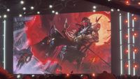 A large screen displays a digital illustration of a character sitting on a throne against a red moon, with a cloaked figure standing to the left.