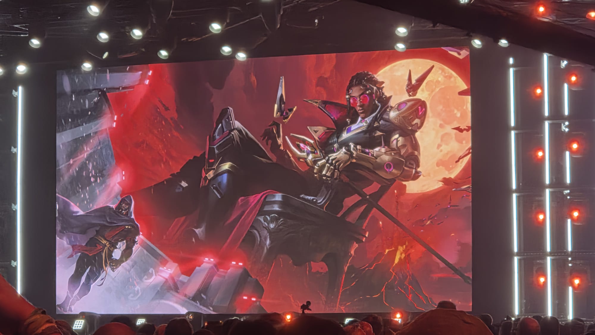 A large screen displays a digital illustration of a character sitting on a throne against a red moon, with a cloaked figure standing to the left.