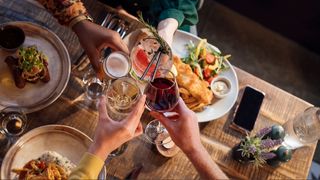 People toasting drinks over a table with meals