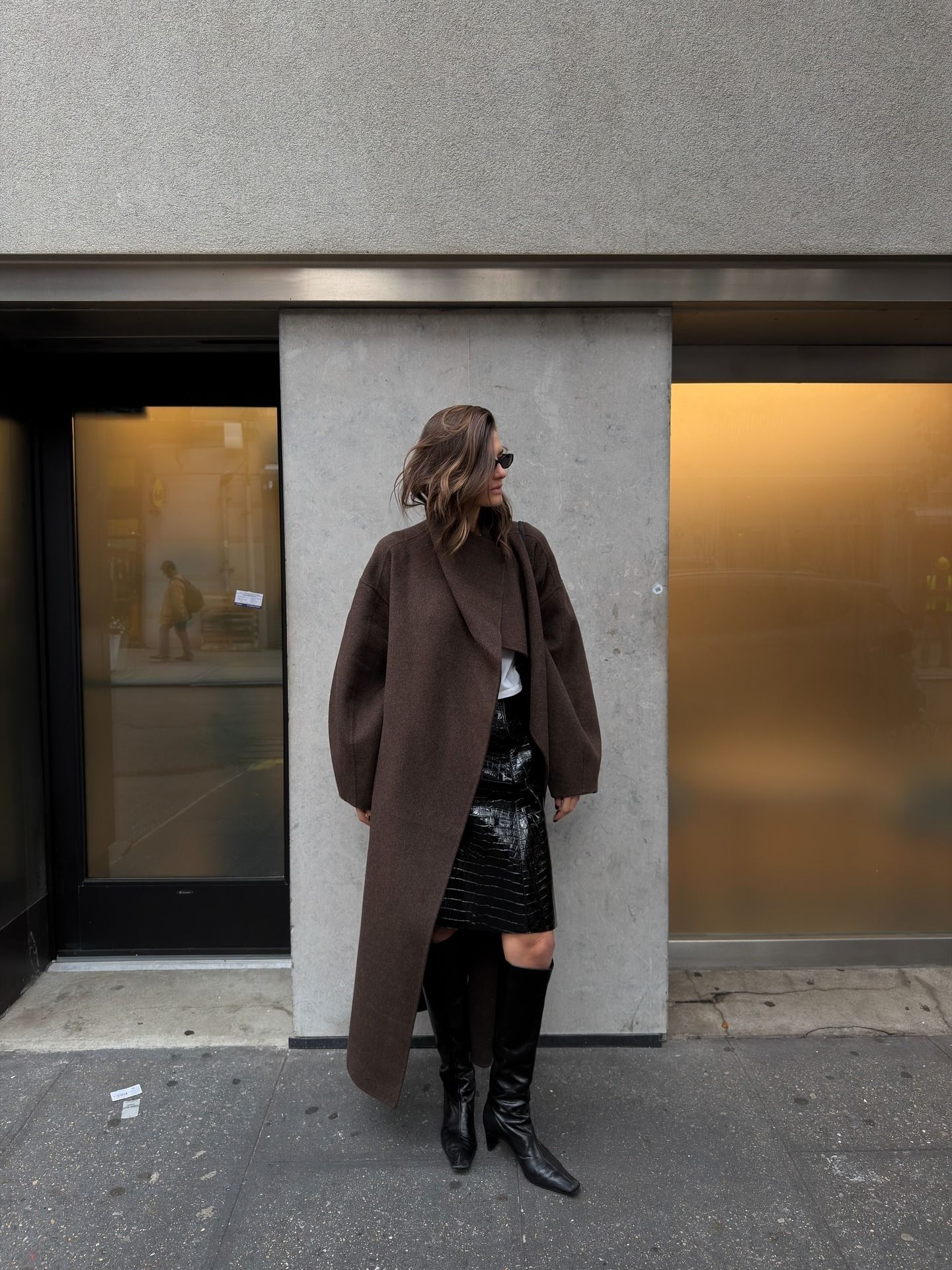 Woman in a brown coat, knee-length skirt and black knee-high boots.