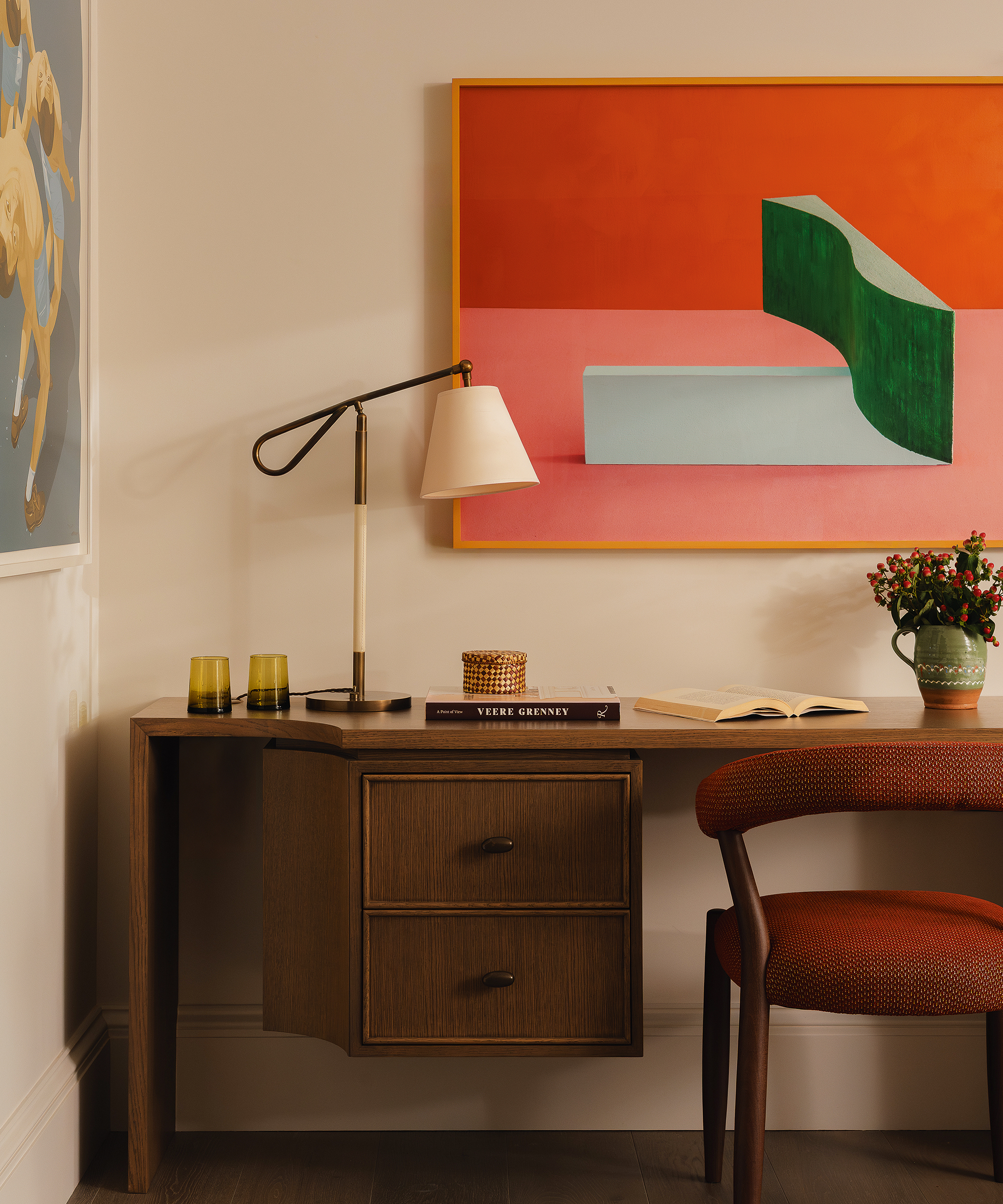 desk in the corner of a room with a red mid century chair and red modern artwork above it