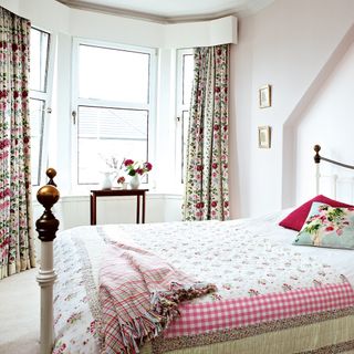 White bedroom with bay window, floral curtains and wrought iron bed