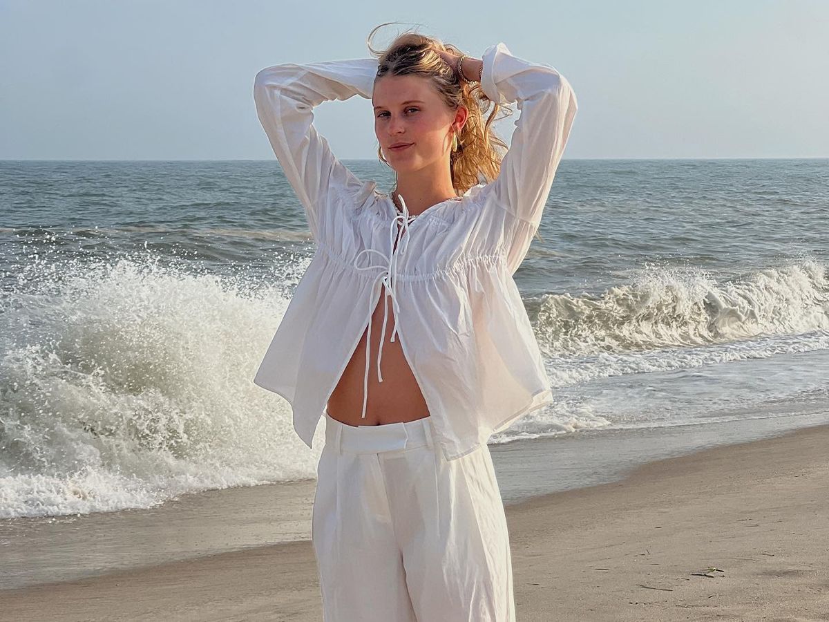 A woman at the beach wearing white linen trousers and a front tie linen long-sleeve top.