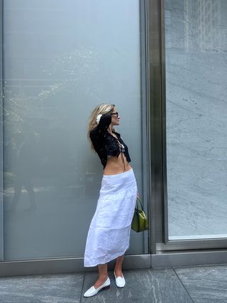 Eliza Huber wearing a black bolero, silver bikini top, white linen skirt, and white heeled loafers from the J.Crew x Maryam Nassir Zadeh collaboration.