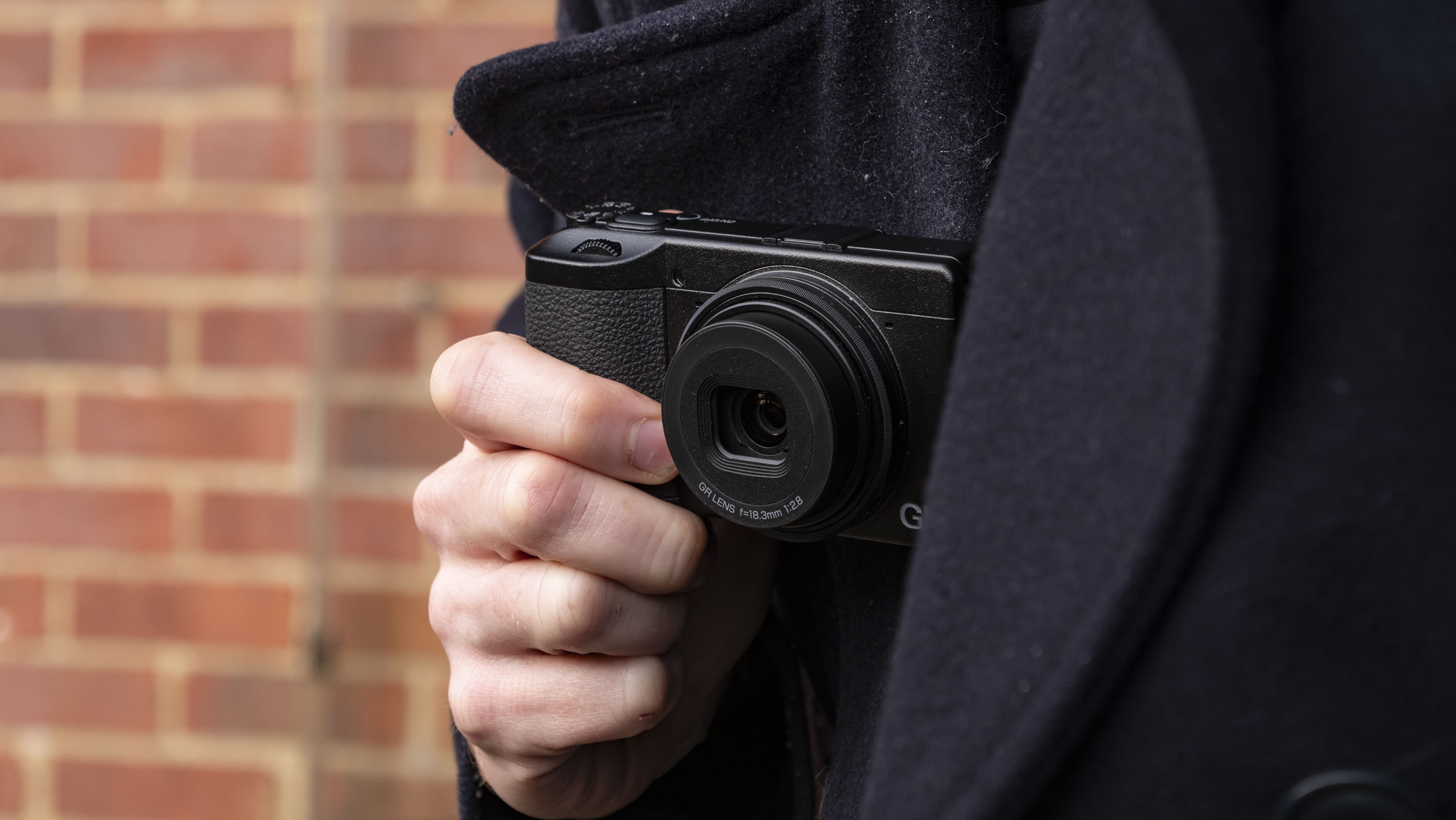 Person holding the Ricoh GR IV compact camera up to their chest