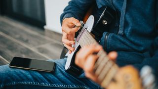 Man playing electric guitar with smartphone on his knee