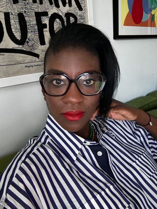 Nikki Ogunnaike wears a striped shirt with red Celine lipstick while sitting on the couch at her house