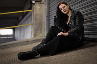 A person sitting in front of a metal shutter, wearing a leather jacket and black boots, taken on the Leica SL3-S with a Leica Summilux SL 50mm f/1.4 Asph lens