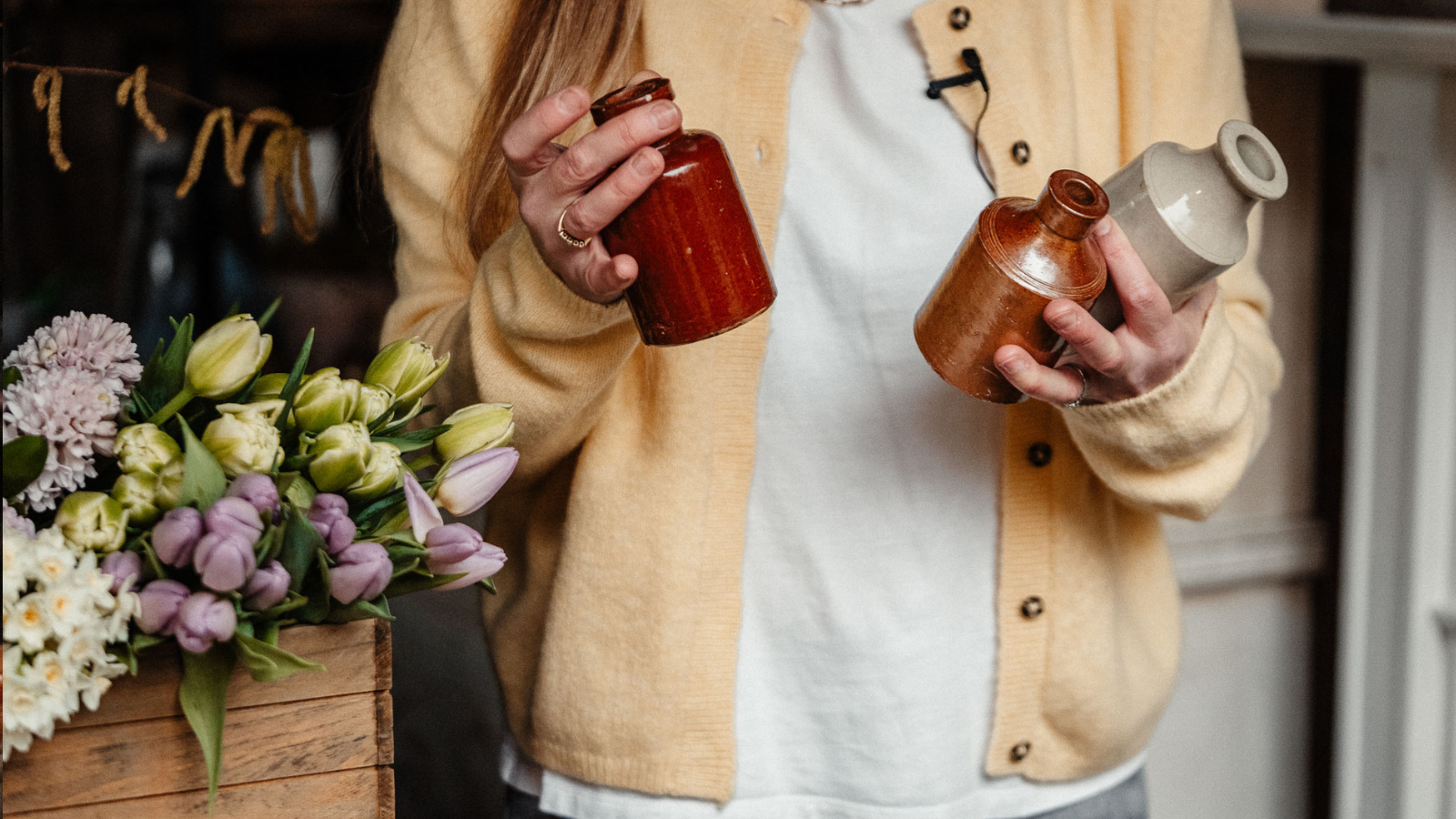 Woman in yellow cardigan holding ceramic ink wells next to spring tulips on a table