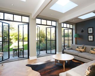 Interior of wraparound extension with corner sofa and coffee table and grey feature wall and steel framed doors to garden