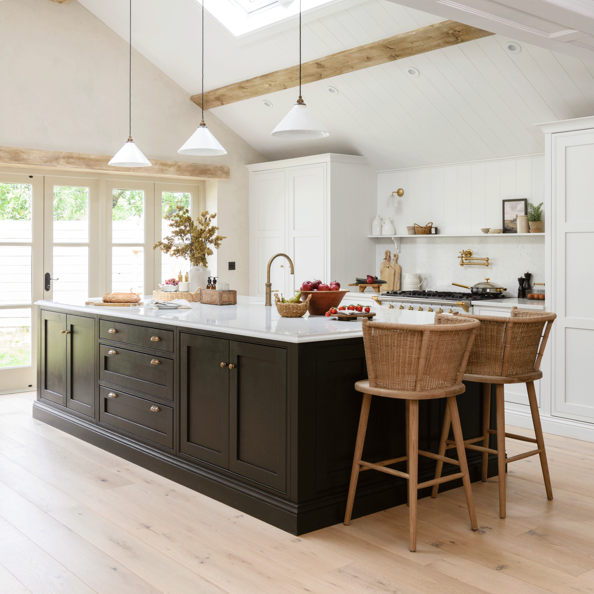 a Shaker kitchen with white cabinets, open shelving and a large black kitchen island with two wicker bar stools