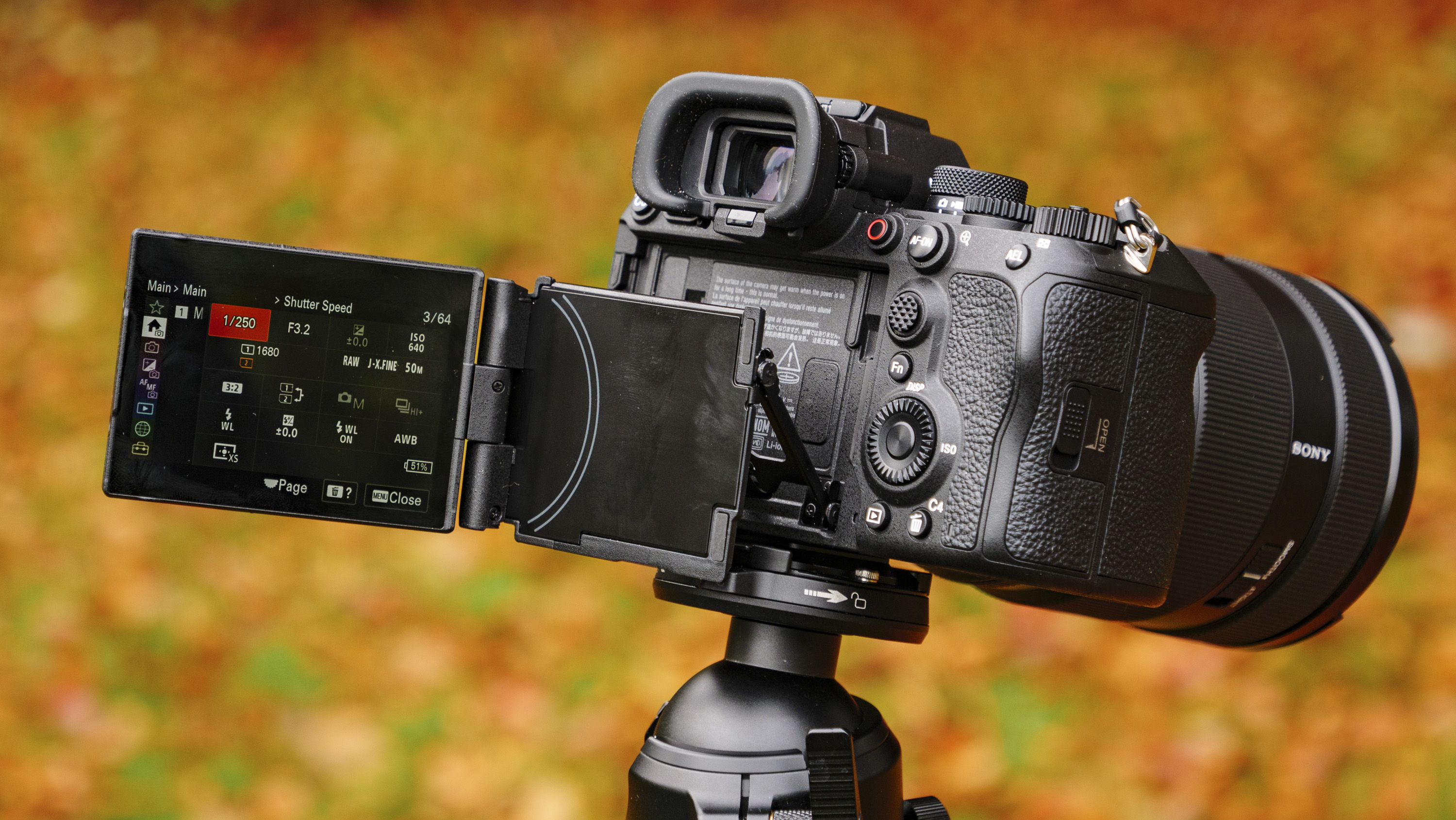 Sony A1 II mirrorless camera's vari-angle screen pulled out to the side, outdoors on a tripod with autumn leaves background