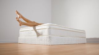 A woman dangles her legs off a mattress that has been placed directly onto the floor