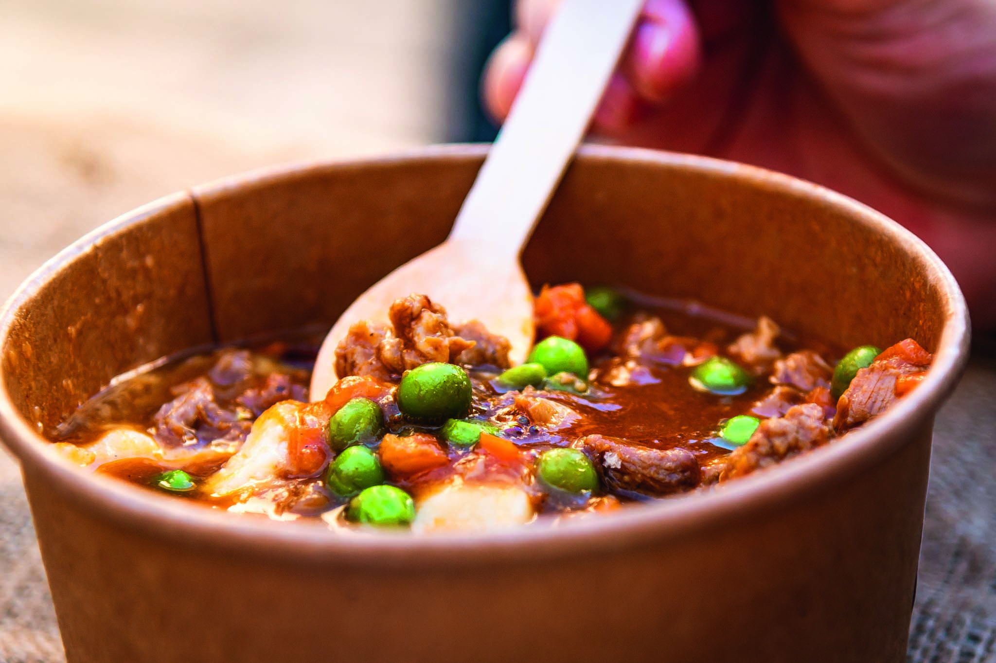 A lamb &amp;amp; green pea stew in cardboard bowl with a spoon