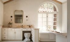 A limewash bathroom with a white vanity, a stool and a freestanding bathtub