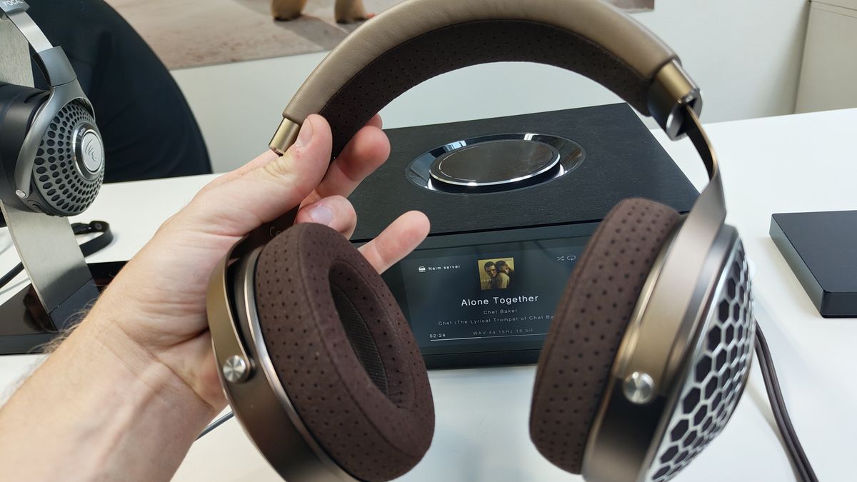 The Focal Clear Mg headphones held at a shallow angle in the hand in front of a music-playing device.