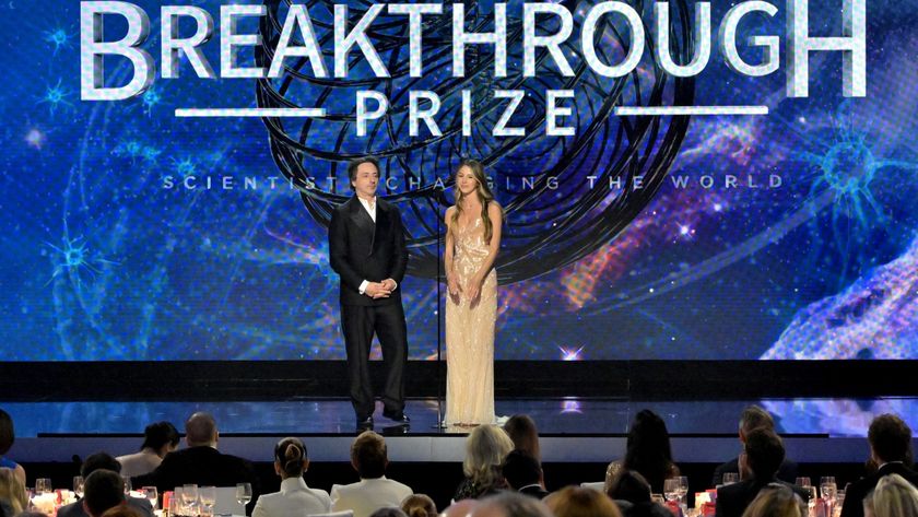 two people stand on stage in a glitzy ballroom awards show