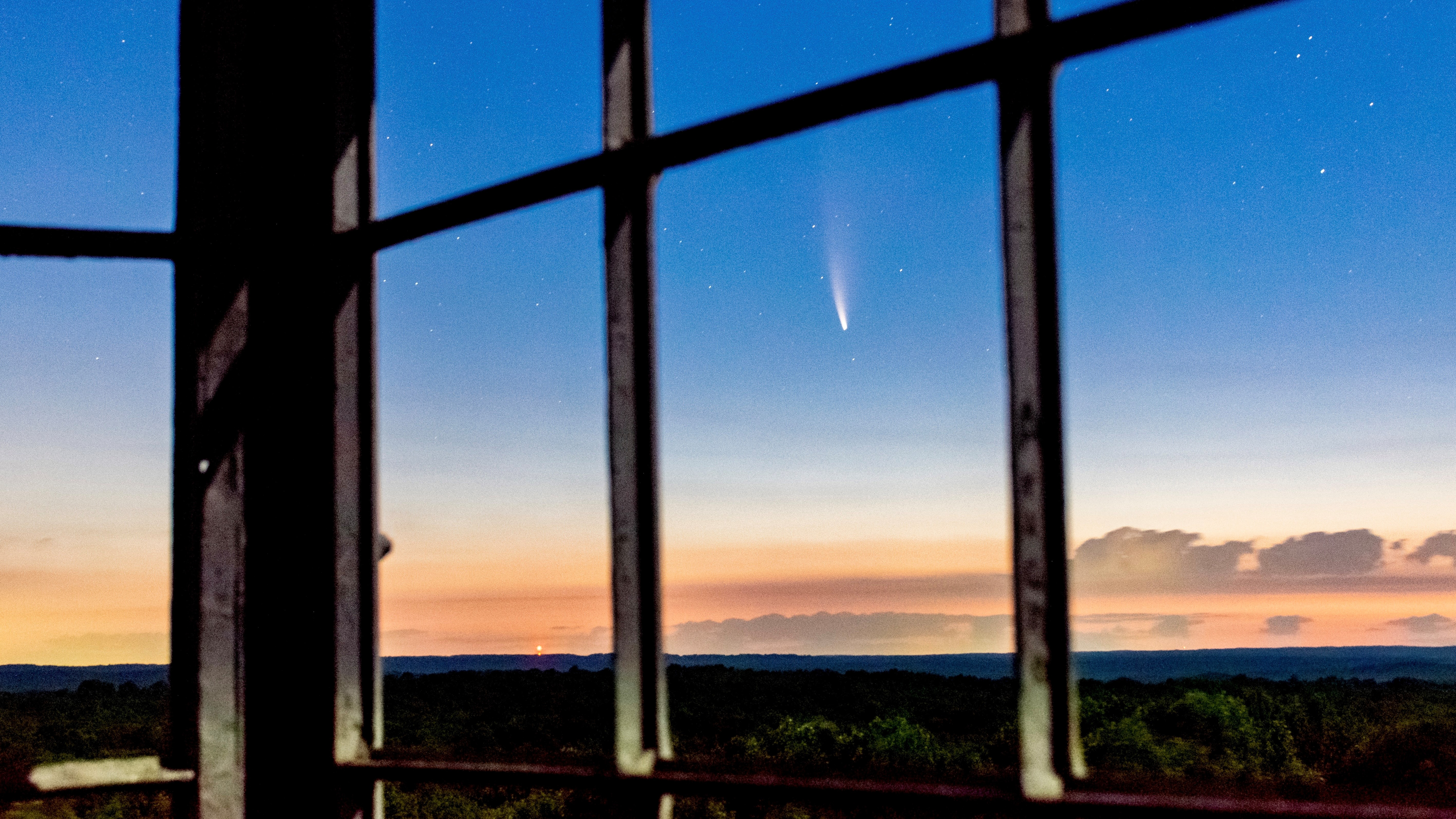 un cometa cruza el cielo sobre un bosque oscuro visto a través de ventanas vacías en lo alto