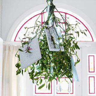Bunch of mistletoe with Christmas cards in hanging in front of stained glass window in hallway