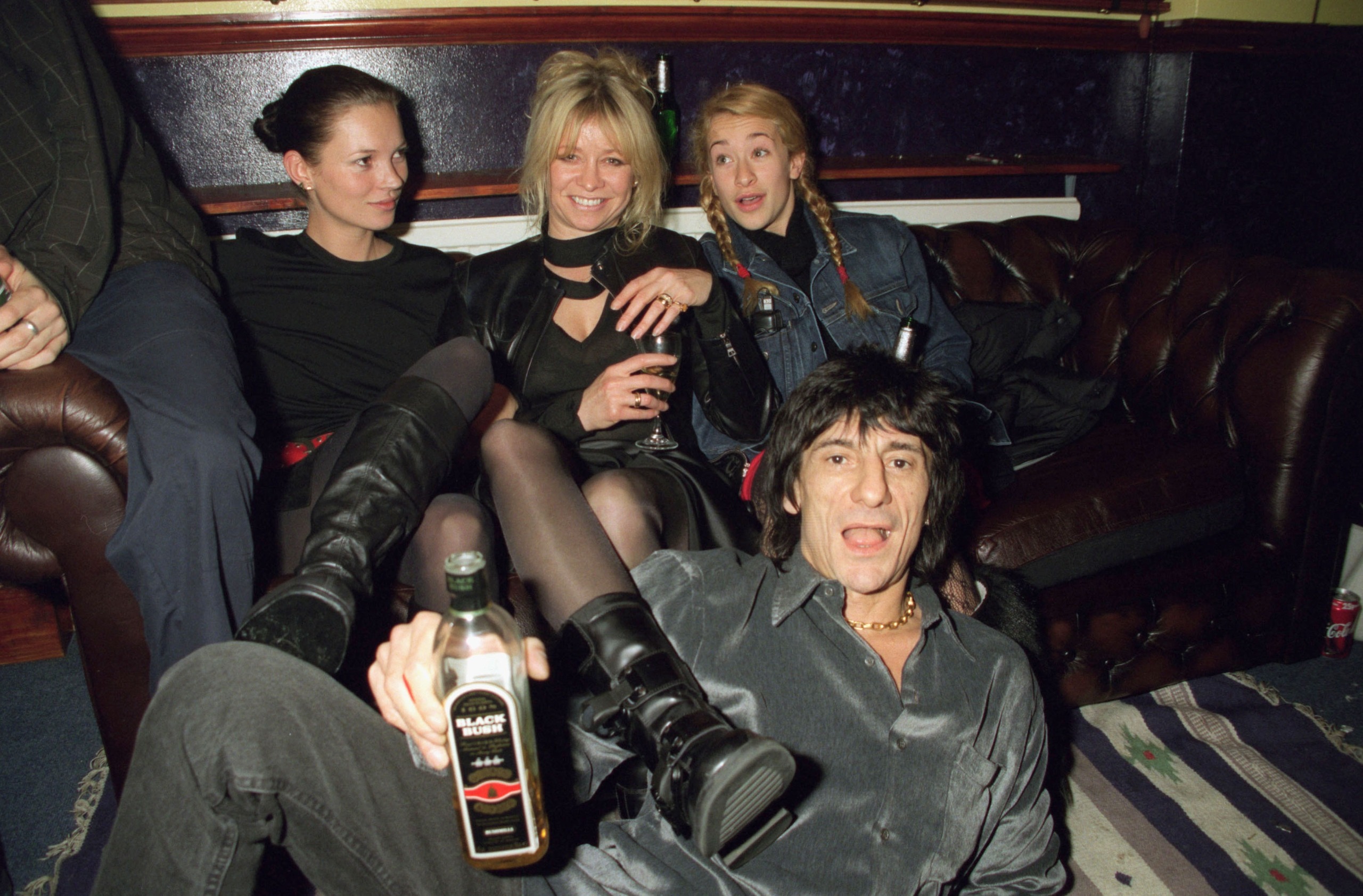 From left to right, Kate Moss, Jo Howard, leah wood and ronnie wood on a sofa. Ronnie is holding a bottle of drink