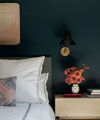 bedroom with dark blue wall, white bedding and vase of pink flowers on nightstand