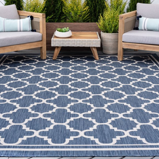 A blue geometric print outdoor rug surrounded by garden furniture.