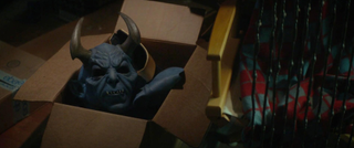 A scary horned blue devil mask sits in a cardboard box looking ominous