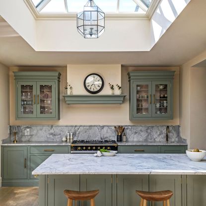 green kitchen cabinetry with sink peninsula and marble worktops