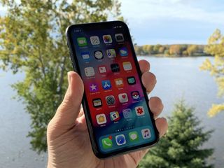 iPhone XR held in hand alongside river