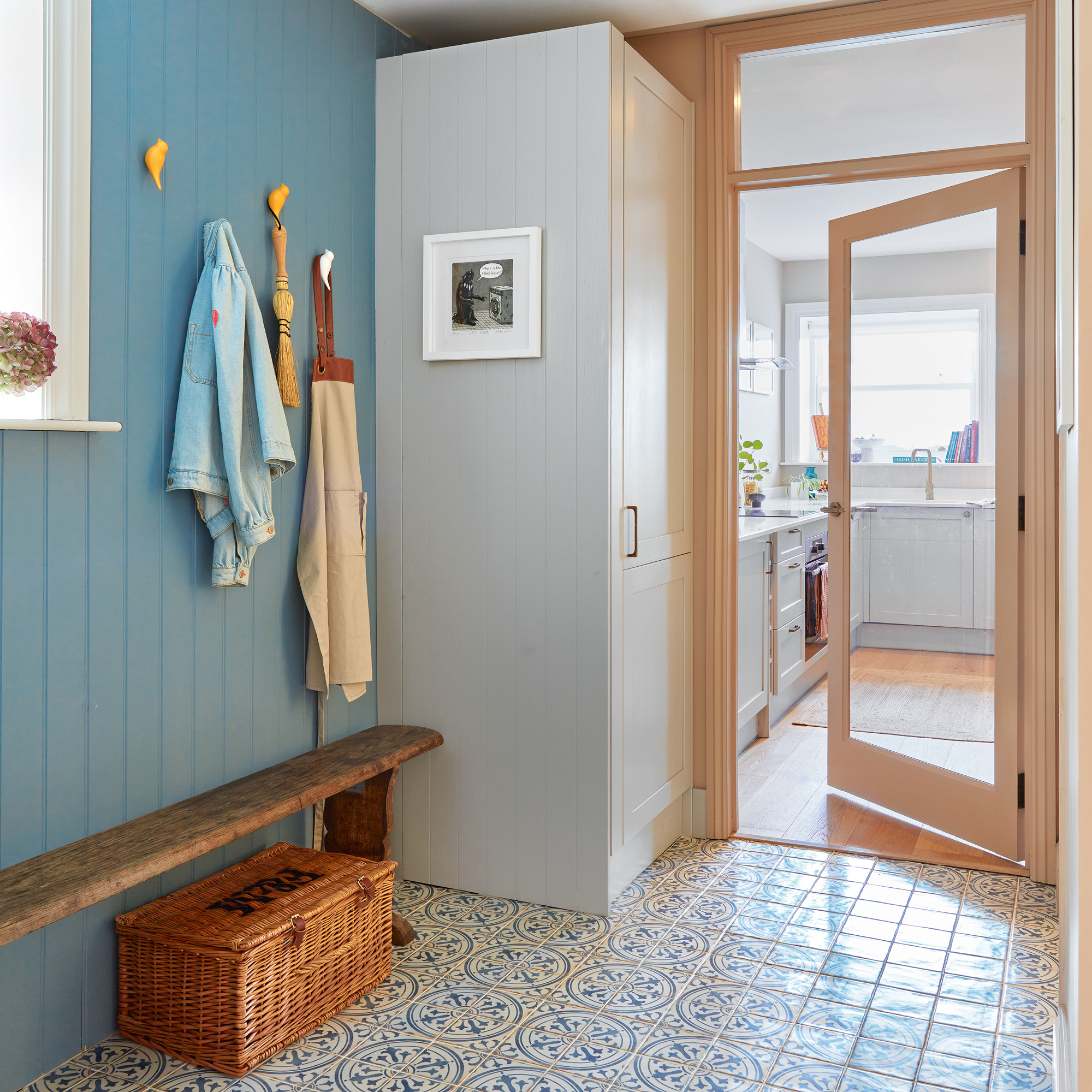 a hallway with patterned tile flooring and teal painted panelling leading into a neutral coloured small kitchen