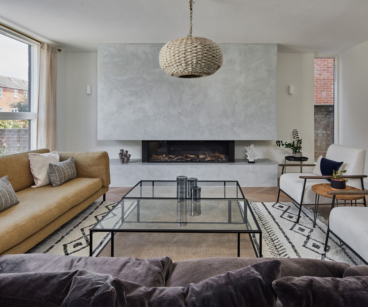 A beautiful contemporary living room with a central glass coffee table and a berber style rug. Matching white armchairs and a sofas