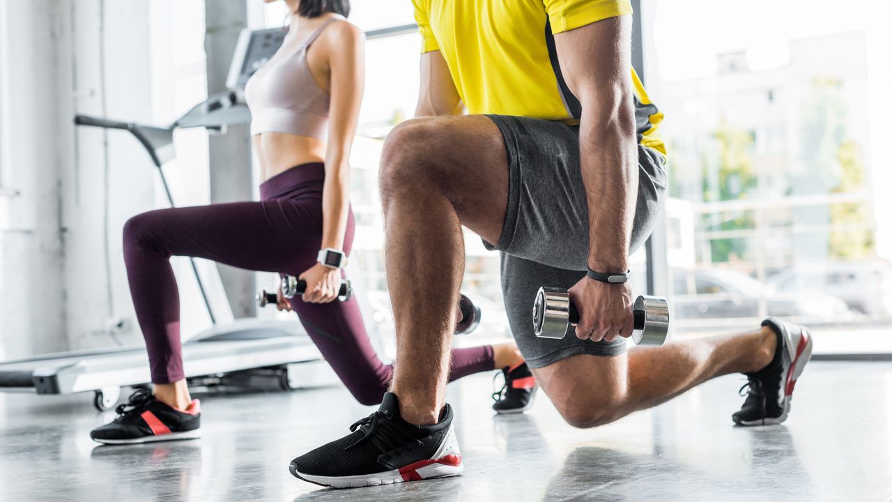 Cropped view of a sportman and sportswoman doing weighted lunges in a brightly lit gym