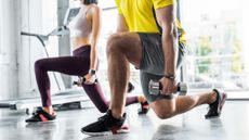 Cropped view of a sportman and sportswoman doing weighted lunges in a brightly lit gym