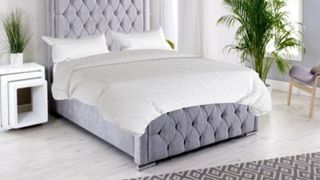 Image shows the The Hilton Bed mattress dressed with a white comforter and placed on a light grey quilted bed frame in a Hilton hotel room