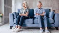 A senior couple sits on a couch looking away from each other.