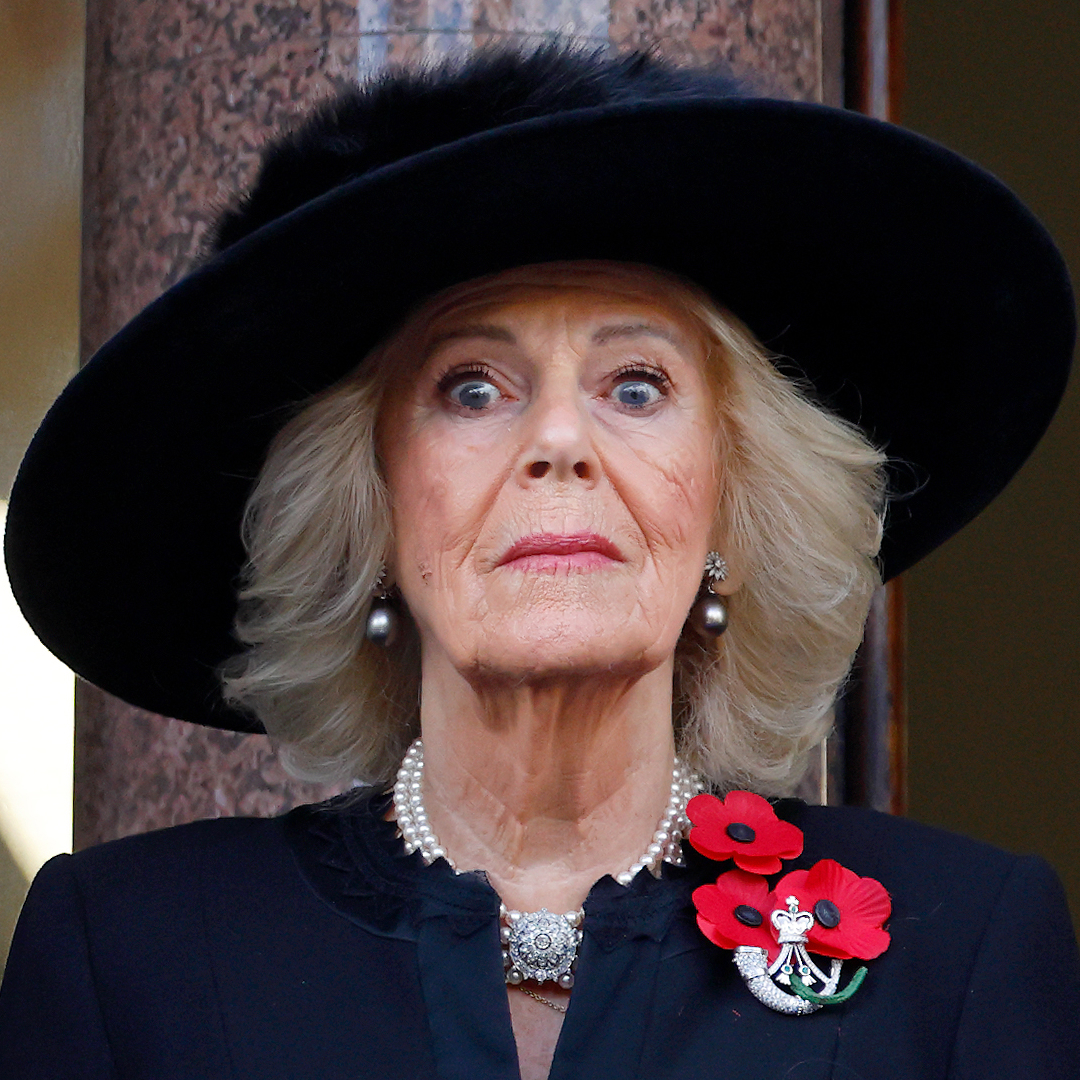 Queen Camilla wearing a black hat and coat with a poppy pin