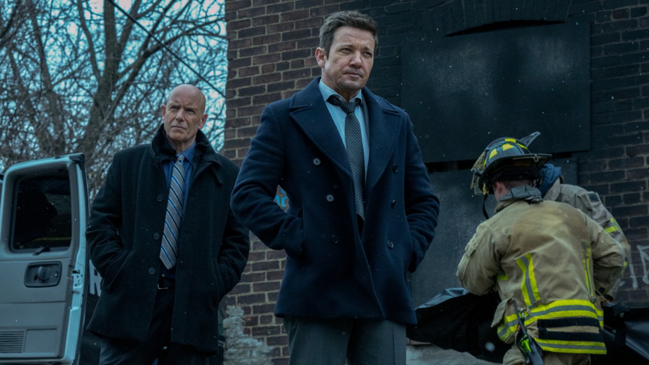 Hugh Dillon and Jeremy Rnner standing with their hands in their pockets in Season 4 of Mayor of Kingstown as firefighters walk behind them. 