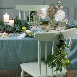 christmas flower arrangement on a green themed table with green tablecloth chairs and plates with white candles flickering