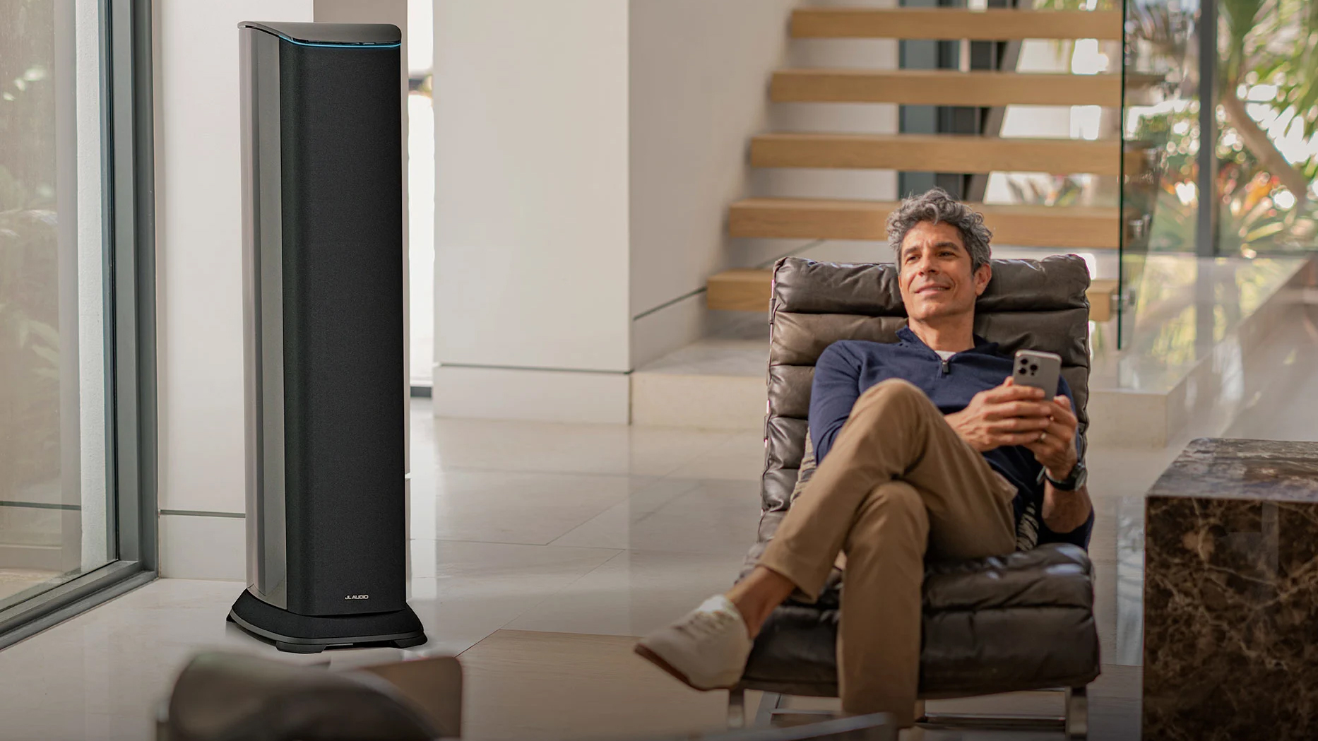 A man sits in a modernist living room next to a very large loudspeaker, which is the JL Audio Primacy T6