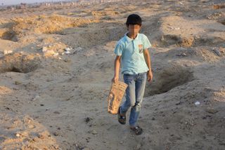A tired child, carrying an artifact he has found, walks between the pits at Albusir El-Malek.