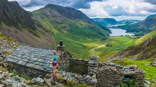 Woman trail runner overlooking mountain valley bothy in the Lake District