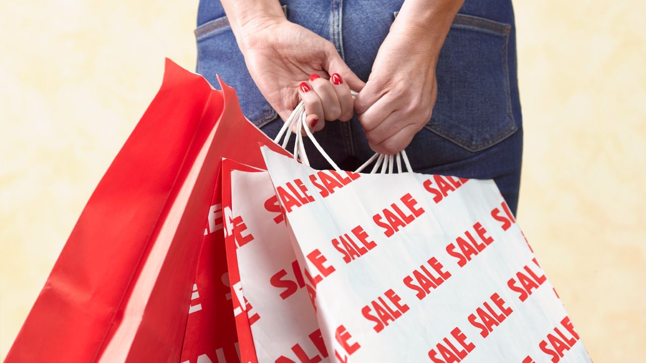 Woman holding plethora of shopping bags behind her bag, some of which say &quot;SALE&quot; on them