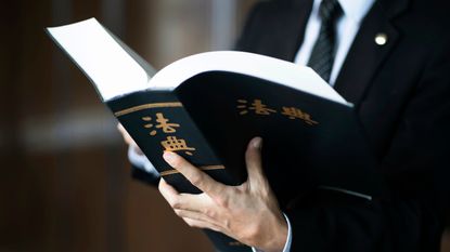 A suited man visible from the shoulders down holding a legal book with Chinese characters on the cover