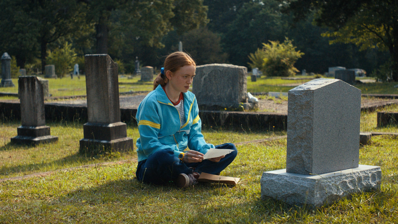 Max sits in front of Billy's grave during the day time in Stranger Things season 4