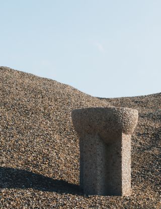 View of a table made of stone aggregate by Vaust pictured outside on stone covered ground under a clear blue sky