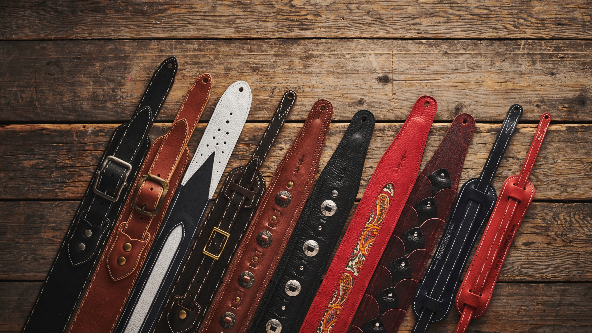A selection of guitar straps lying on a wooden floor