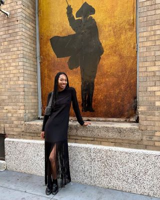 Woman wears a black dress with fringe, The Row loafers and black ankle socks.