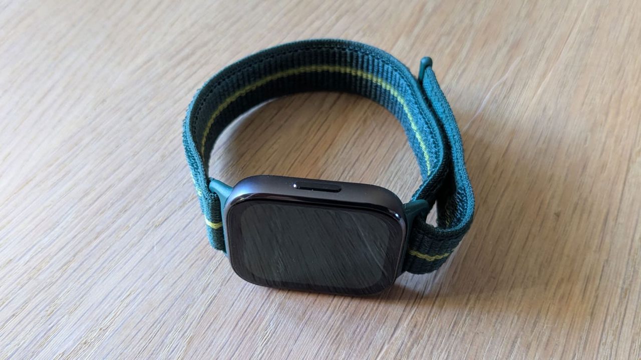 The Motorola Moto Fit Watch on a wooden table, picture taken from a bird's eye view to show the side button.